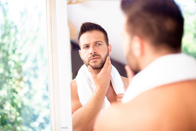 Handsome man looking at his reflection in the mirror while he touches his face